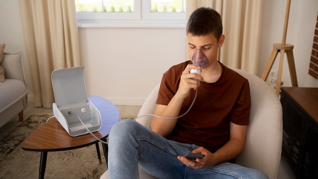 Vista de un adolescente que usa nebulizador en casa por problemas de salud respiratoria