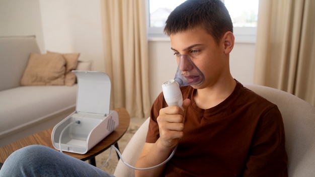 Foto gratuita vista de un adolescente que usa nebulizador en casa por problemas de salud respiratoria
