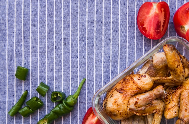 Vista aérea de alitas de pollo asadas con tomate y chiles verdes contra un mantel azul