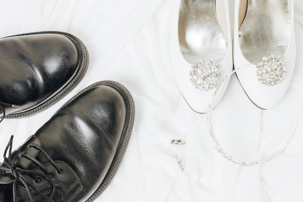 Una vista aérea de los anillos de boda; Corona y zapatos en tela blanca.