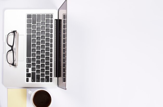 Una vista aérea de anteojos en una computadora portátil con una nota adhesiva y una taza de café sobre fondo blanco