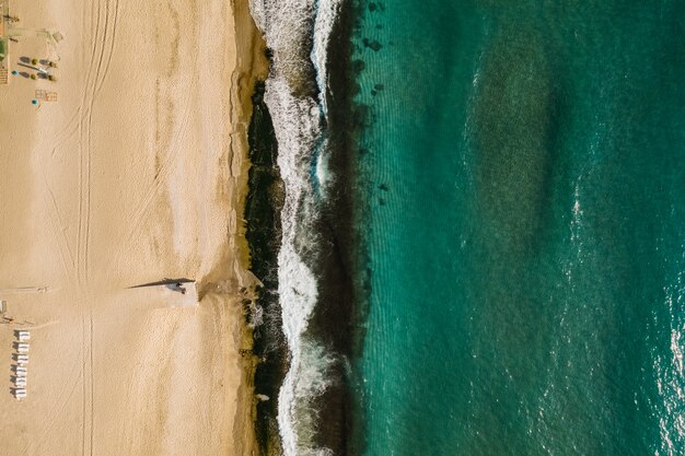 Vista aérea de arena que se encuentra con el agua de mar y las olas