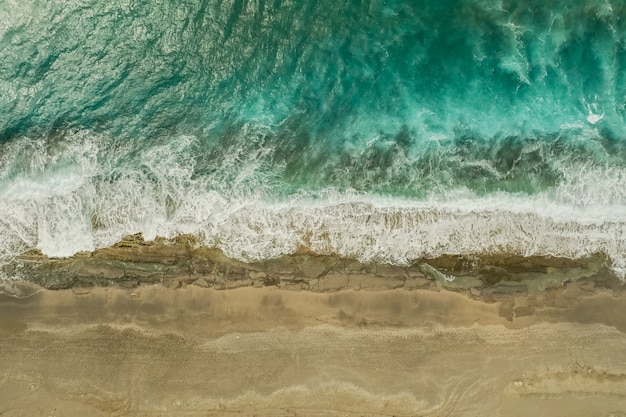 Vista aérea de arena que se encuentra con el agua de mar y las olas