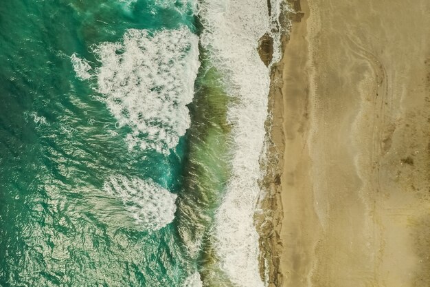 Vista aérea de arena que se encuentra con el agua de mar y las olas