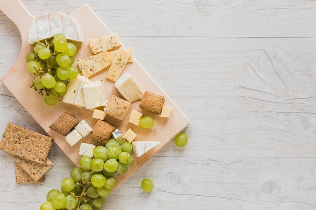 Una vista aérea de bloques de queso, pan crujiente y uvas en el escritorio de madera