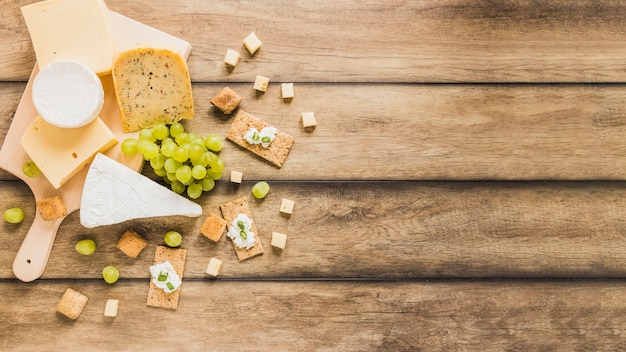 Una vista aérea de bloques de queso; uvas; Pan crujiente con crema de queso en mesa de madera