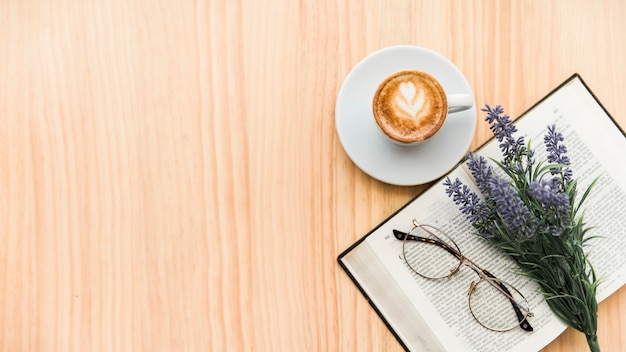 Vista aérea de café con leche, flor de lavanda, gafas y portátil sobre fondo de madera