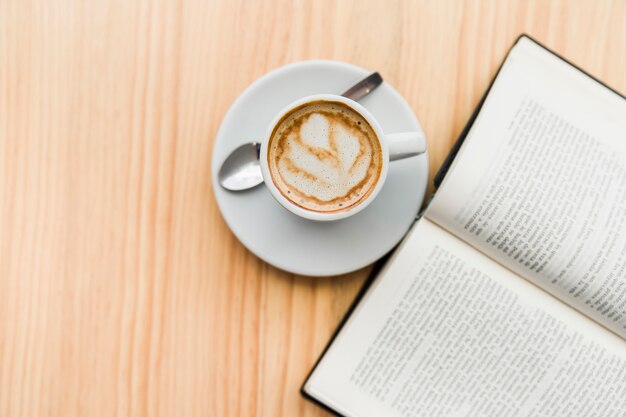 Vista aérea de café con leche y libro abierto en la mesa de madera