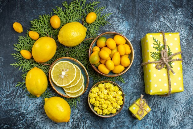 Vista aérea de la caja de regalo amarilla y colección de frutas cítricas frescas orgánicas naturales cortadas y enteras en ramas de abeto una olla con caramelos sobre fondo oscuro