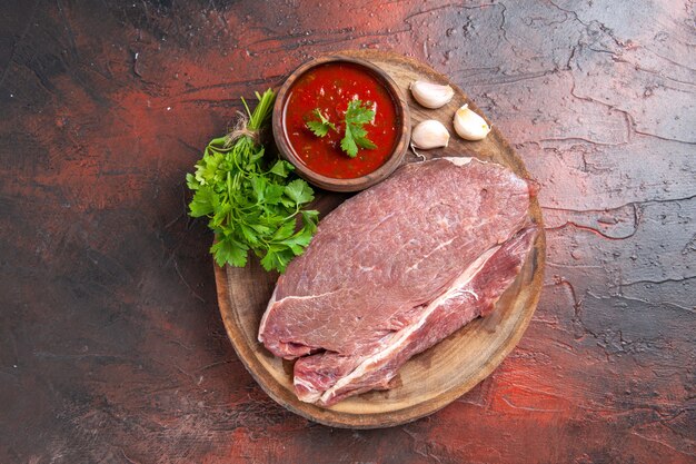 Vista aérea de la carne roja en bandeja de madera y salsa de tomate verde ajo sobre fondo oscuro