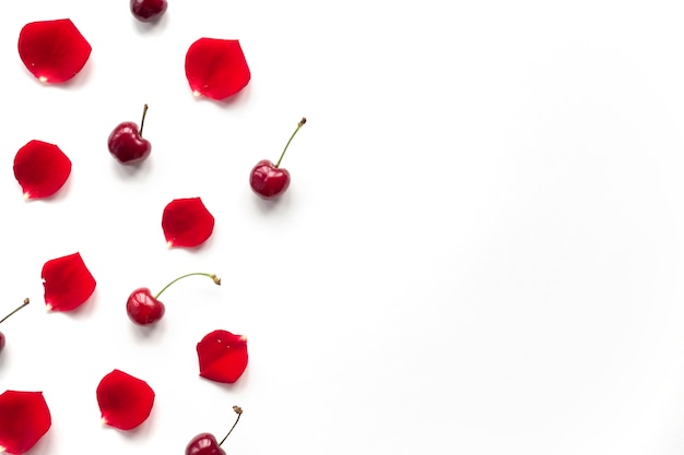 Vista aérea de cereza y pétalos de rosa sobre fondo blanco