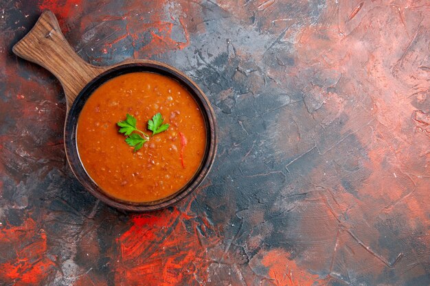 Vista aérea de la clásica sopa de tomate sobre una tabla de cortar marrón sobre una tabla de colores mezclados