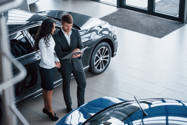 Vista aérea. Clienta y empresario barbudo con estilo moderno en el salón del automóvil