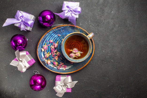 Vista aérea de coloridos regalos y accesorios de decoración una taza de té negro sobre fondo oscuro