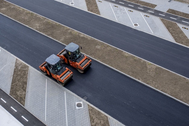Vista aérea del compactador de rodillos de asfalto vibratorio naranja sobre un pavimento nuevo