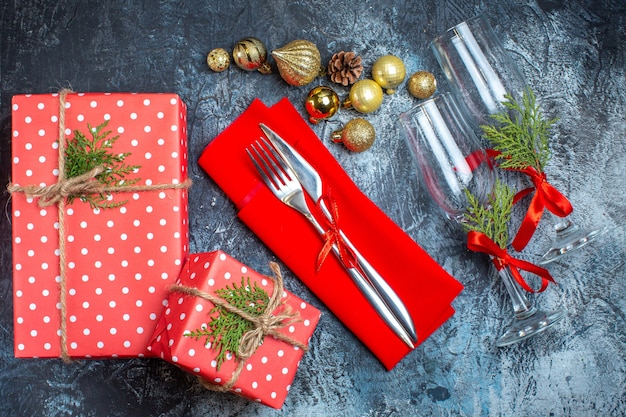 Vista aérea de las copas de cristal caídas y cubiertos, caja de regalo de accesorios de decoración y calcetín de navidad sobre fondo oscuro