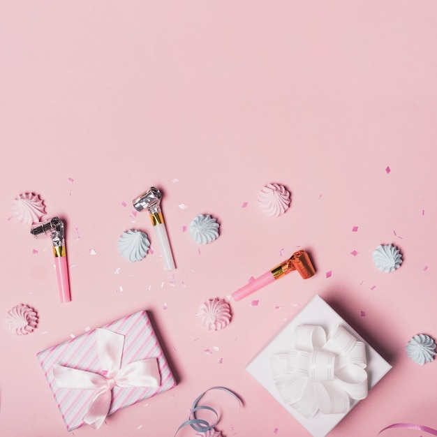 Foto gratuita vista aérea de crema batida; papel picado; soplador de fiesta y cajas de regalo en fondo rosa