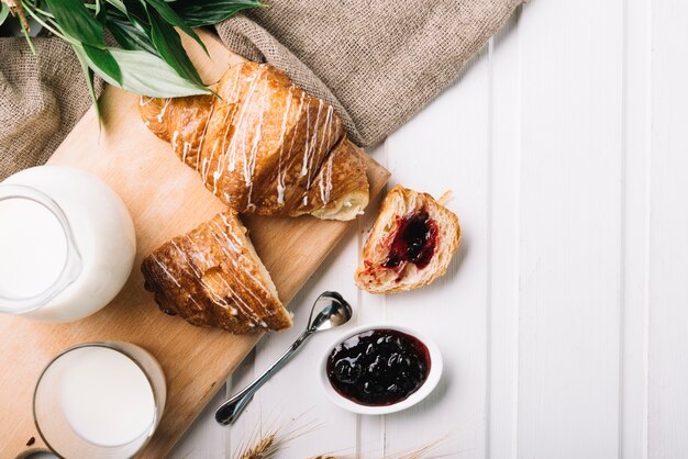 Vista aérea de croissant relleno de mermelada de bayas y vaso de leche en la mesa