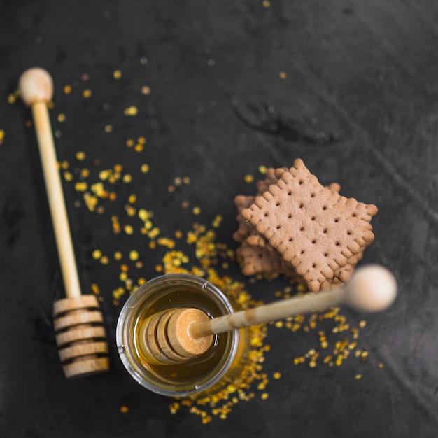 Una vista aérea del cucharón de madera en la olla de miel con pila de galletas y polen de abeja