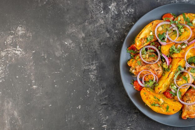 Vista aérea de una deliciosa cena con pollos, papas verdes en una cacerola en un plato gris en el lado izquierdo sobre fondo de color oscuro con espacio libre