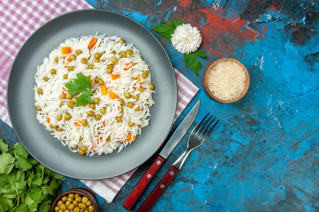 Vista aérea de una deliciosa comida de arroz con zanahoria pisum sobre una toalla morada y cubiertos sobre fondo azul.