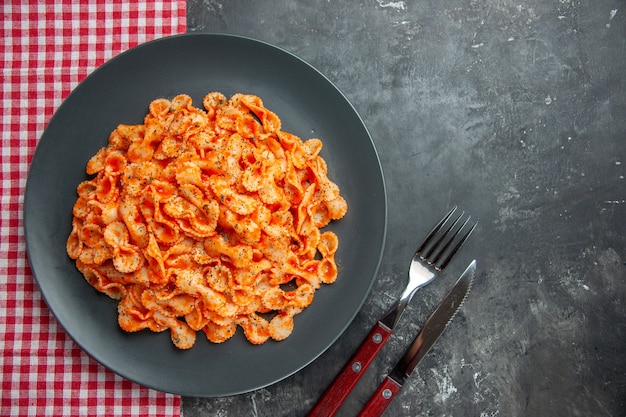 Vista aérea de una deliciosa comida de pasta en un plato negro para cenar sobre una toalla y cubiertos rojos sobre fondo oscuro