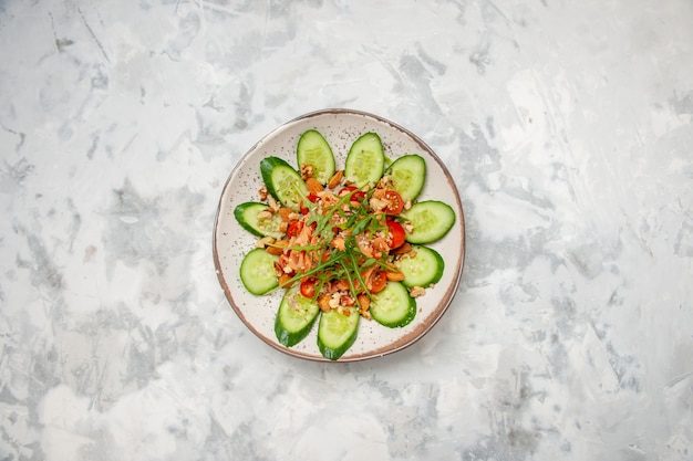 Vista aérea de una deliciosa ensalada decorada con pepino picado y verduras sobre una superficie blanca manchada con espacio libre