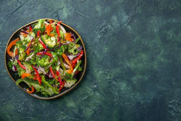 Vista aérea de una deliciosa ensalada vegana en un plato con varias verduras frescas en el lado derecho sobre fondo oscuro