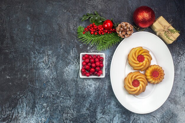 Vista aérea de deliciosas galletas en un plato blanco y decoraciones de año nuevo cornel de regalo en una olla pequeña sobre una superficie oscura