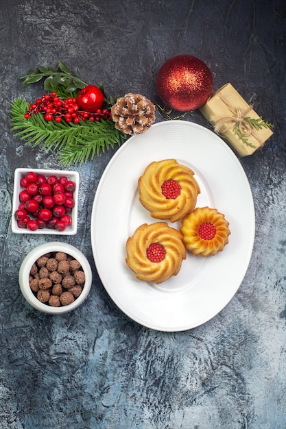 Vista aérea de deliciosas galletas en un plato blanco y decoraciones de año nuevo cornel de regalo en una pequeña olla de chocolate sobre una superficie oscura