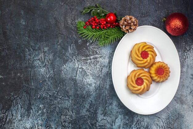 Vista aérea de deliciosas galletas en un plato blanco y decoraciones de año nuevo superficie oscura