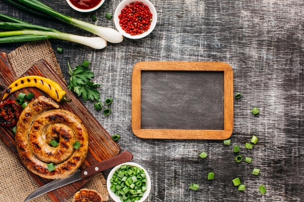 Vista aérea de deliciosas salchichas a la parrilla y un ingrediente fresco con pizarra en blanco sobre fondo de madera