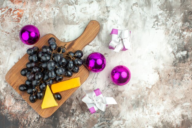 Vista aérea del delicioso racimo de uva negra fresca y queso sobre tabla de cortar de madera y accesorios de decoración de regalos sobre fondo de colores mezclados