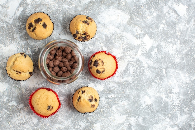 Vista aérea de deliciosos cupcakes pequeños y chocolate en una olla de vidrio en el lado derecho de la mesa de hielo