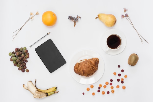 Una vista aérea del diario y la pluma con frutas; Café y croissant aislado sobre fondo blanco