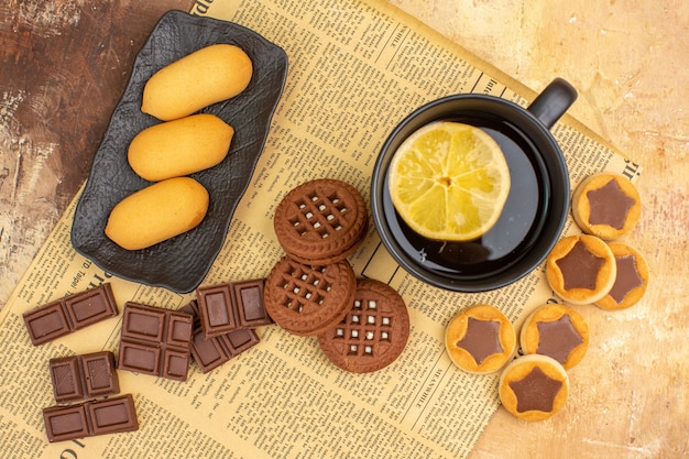 Vista aérea de diferentes galletas y té en una taza negra sobre una mesa de colores mezclados