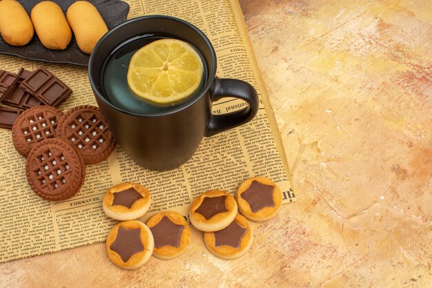 Vista aérea de diferentes galletas y té en una taza negra sobre una mesa de colores mezclados