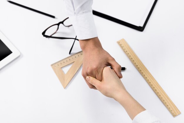 Vista aérea de dos empresarios que se dan la mano sobre el escritorio blanco.