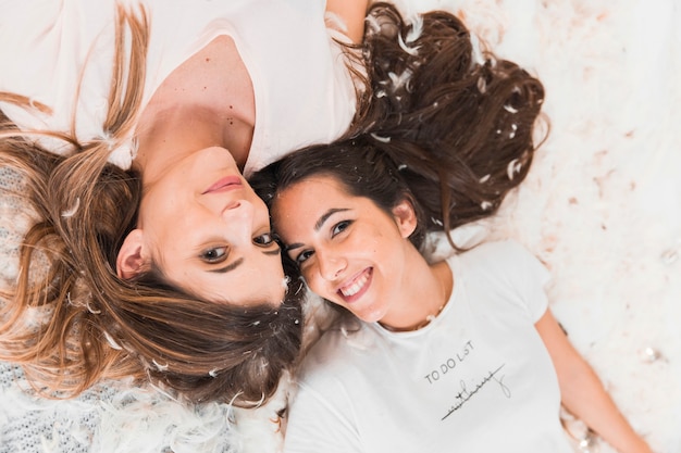 Una vista aérea de dos mujeres sonrientes que mienten sobre plumas suaves