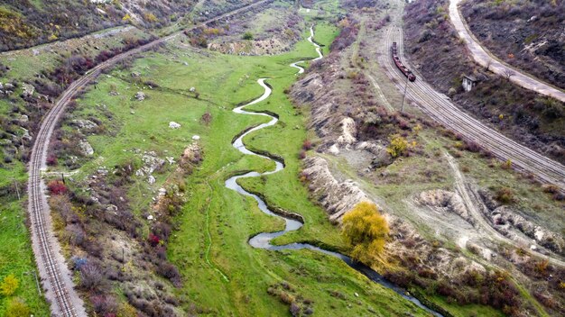 Vista aérea de drone de la naturaleza en Moldavia, fluye la corriente que fluye hacia el barranco, pendientes con escasa vegetación y rocas, tren en movimiento, cielo nublado