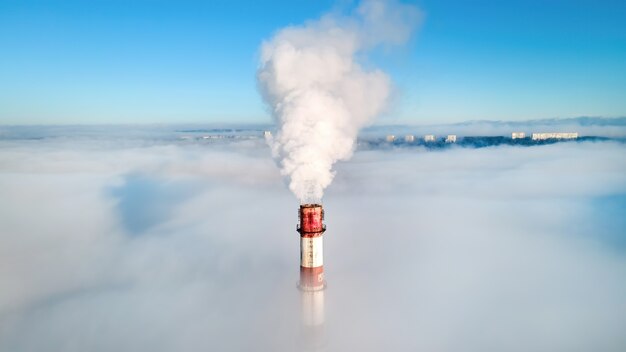 Vista aérea de drone del tubo de la estación termal visible sobre las nubes con humo saliendo.