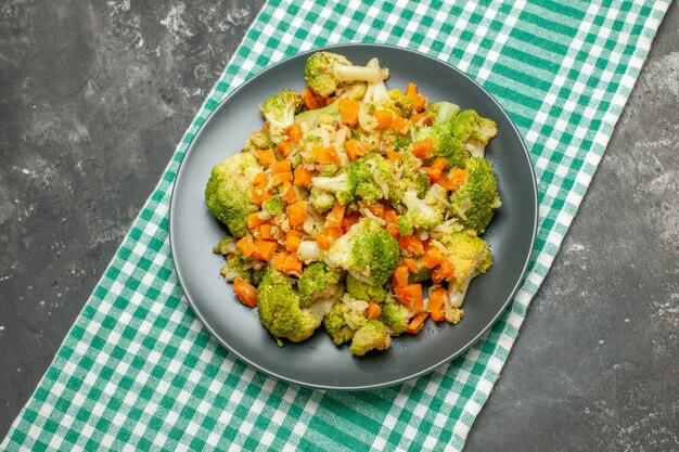 Vista aérea de ensalada de verduras saludables en una toalla despojada verde sobre la mesa gris