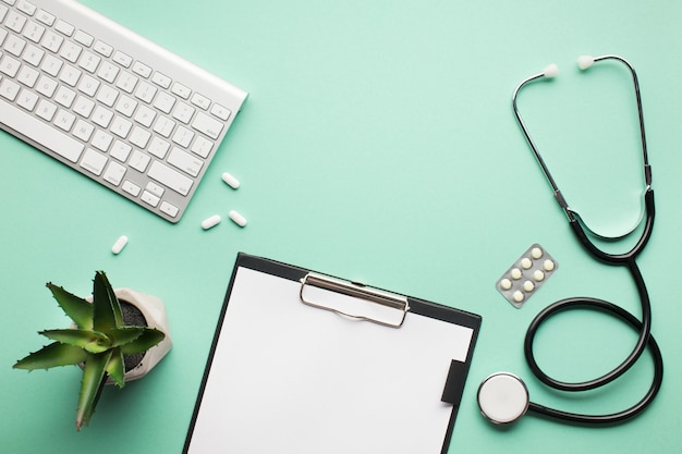 Vista aérea del escritorio médico con planta suculenta y teclado inalámbrico en superficie verde