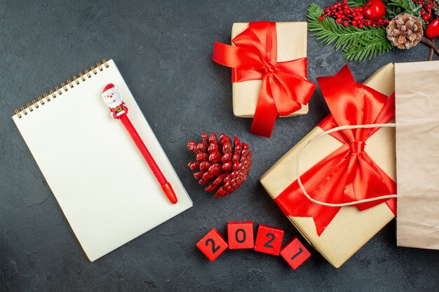 Vista aérea del estado de ánimo navideño con conos de coníferas y ramas de abeto de regalo junto al cuaderno en la mesa oscura