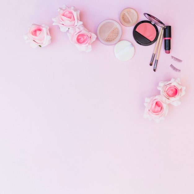 Una vista aérea de flores falsas con productos cosméticos sobre fondo rosa
