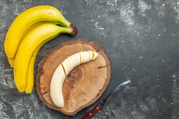 Foto gratuita vista aérea fuente de nutrición paquete de plátanos frescos y picados en un cuchillo de tabla de cortar de madera sobre fondo gris