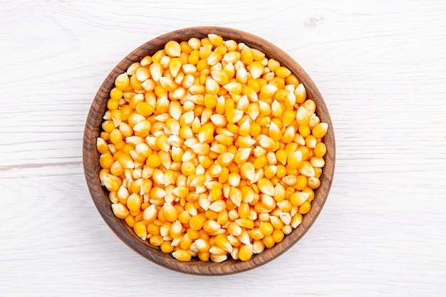 Vista aérea de granos de maíz frescos en un recipiente marrón sobre fondo blanco.