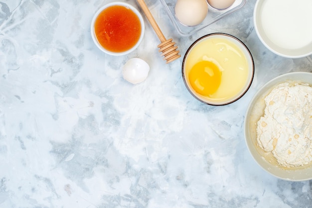 Vista aérea de harina blanca en un tazón y una herramienta de cocina de acero inoxidable, huevos rotos enteros en el lado izquierdo sobre una superficie de dos tonos