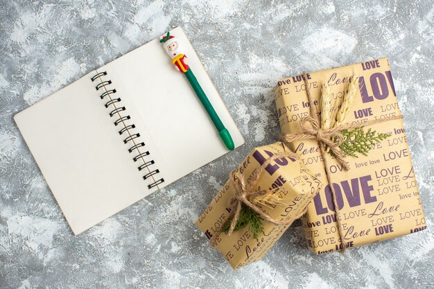 Vista aérea de hermosos regalos llenos de Navidad grandes y pequeños y cuadernos abiertos con lápiz sobre la mesa de hielo