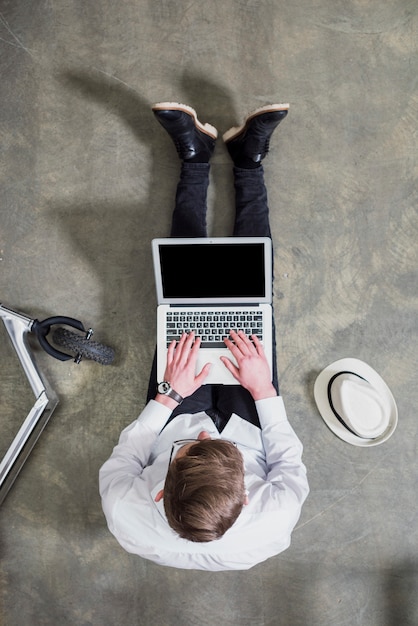 Una vista aérea de hombre joven sentado en el piso de concreto usando laptop